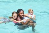 camp counselor smiles while two young campers hang with her in the pool