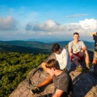 Several teens sit on top of rock at sunset with a beautiful view.