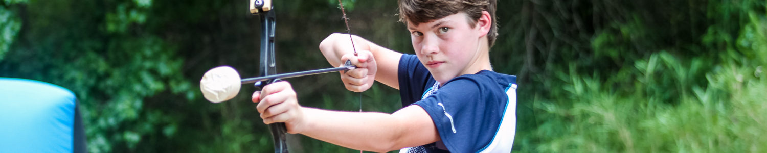 A boy in a blue and white shirt prepares to shoot an arrow during a game of archery tag.