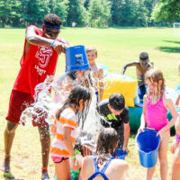 A camp counselor dumps a bucket of water over a campers head.