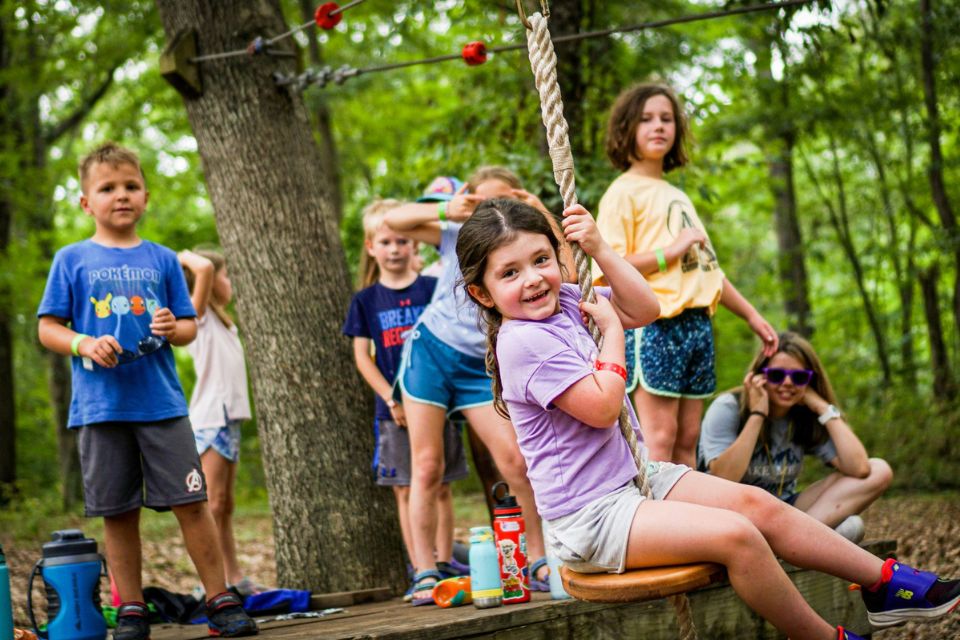 junior day camper in purple shirt rides zipline on the playground at Camp Canaan