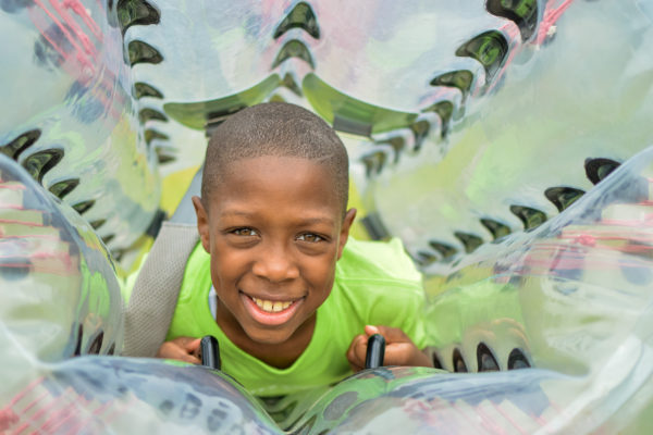 A young boy smiles looking through the center of his bubble soccer ball.