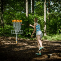 A woman makes a short putt on the disc golf course at Camp Canaan.