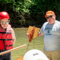 A man in a Michigan State tee shirt holds a homemade paddle during a team building exercise at Camp Canaan.