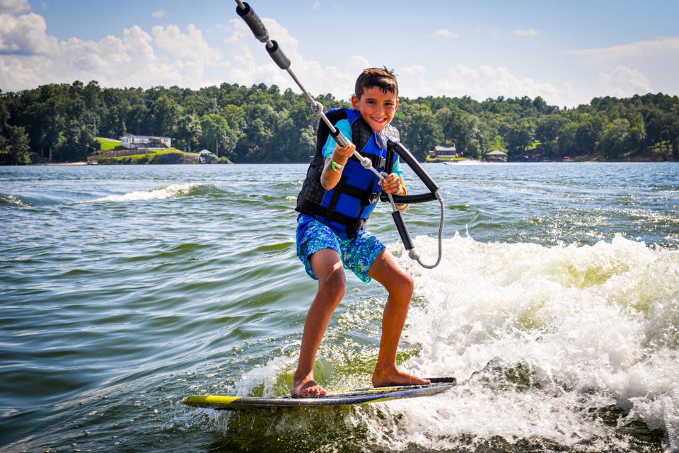 male camper smiles while wakeboarding behind a boat on Lake Wylie