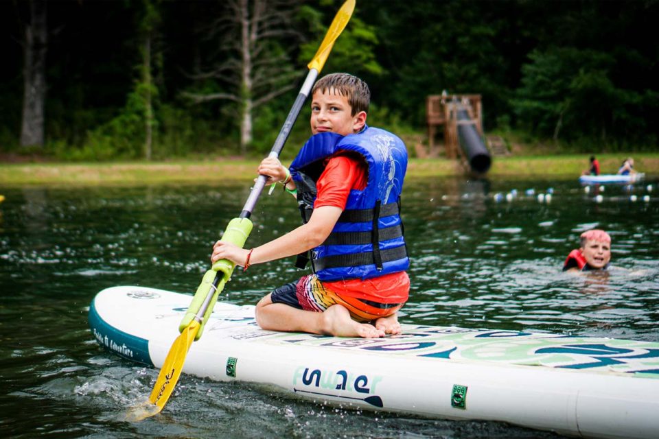 camper sits on stand up paddle board while paddling across Lake Canaan