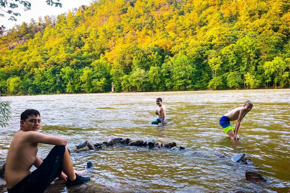 TLC campers enjoy wading in the water against a backdrop of beautiful trees with fall-colored leaves