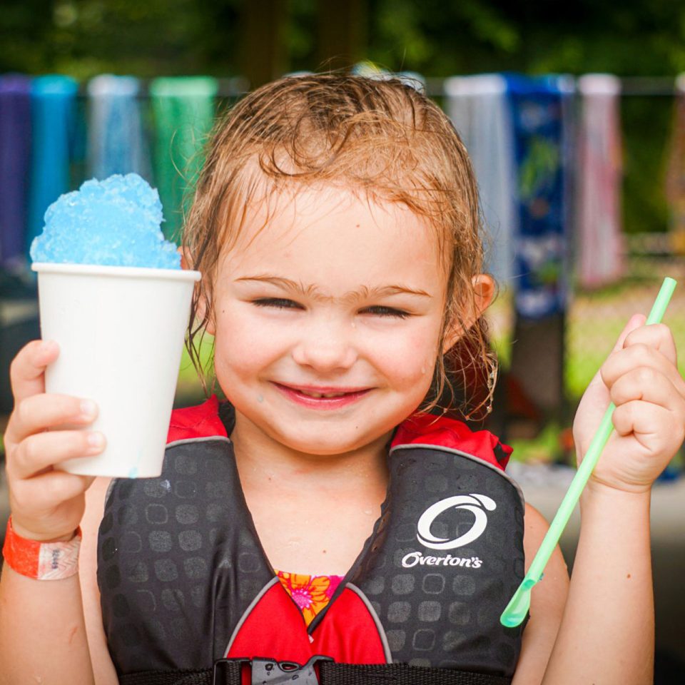 junior day camper smiles while holding a straw and blue frozen icy treat