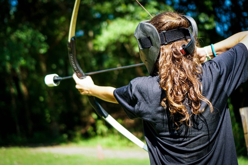 girl with mask and curly brown hair tees up archery tag arrow in the bow