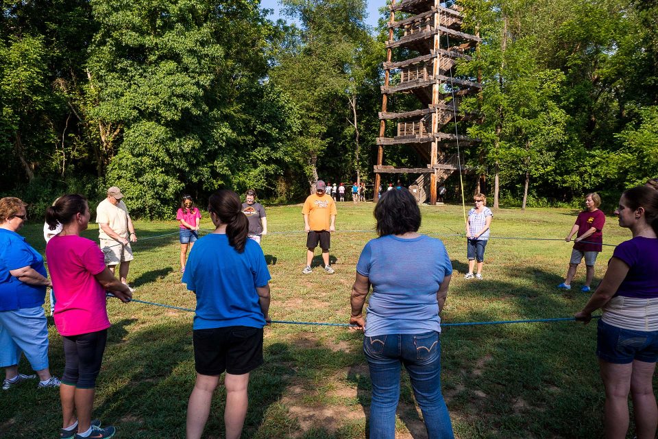 team building group circles up holding a rope in front of the Zipline Canopy Tour tower at Canaan