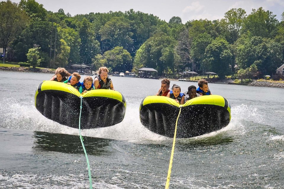 two groups of four kids tube side-by-side behind the boat in Lake Wylie trying to hold on