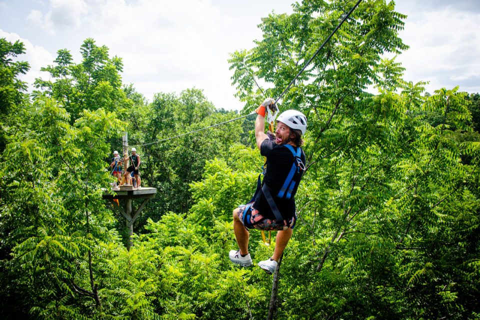 man sticks out tongue while zipping towards Zipline Canopy Tour platform at Camp Canaan