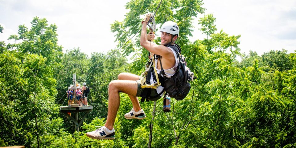 young man in white helmet zips from platform to platform on the Zipline Canopy Tour at Camp Canaan