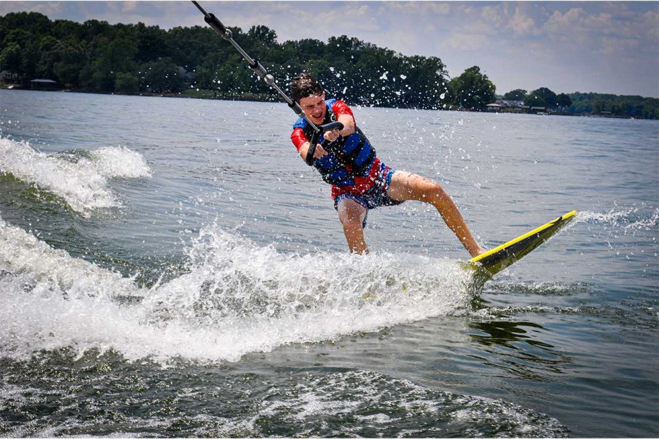 older camper wakeboards behind the boat on Lake Wylie during co-ed overnight camp at Camp Canaan