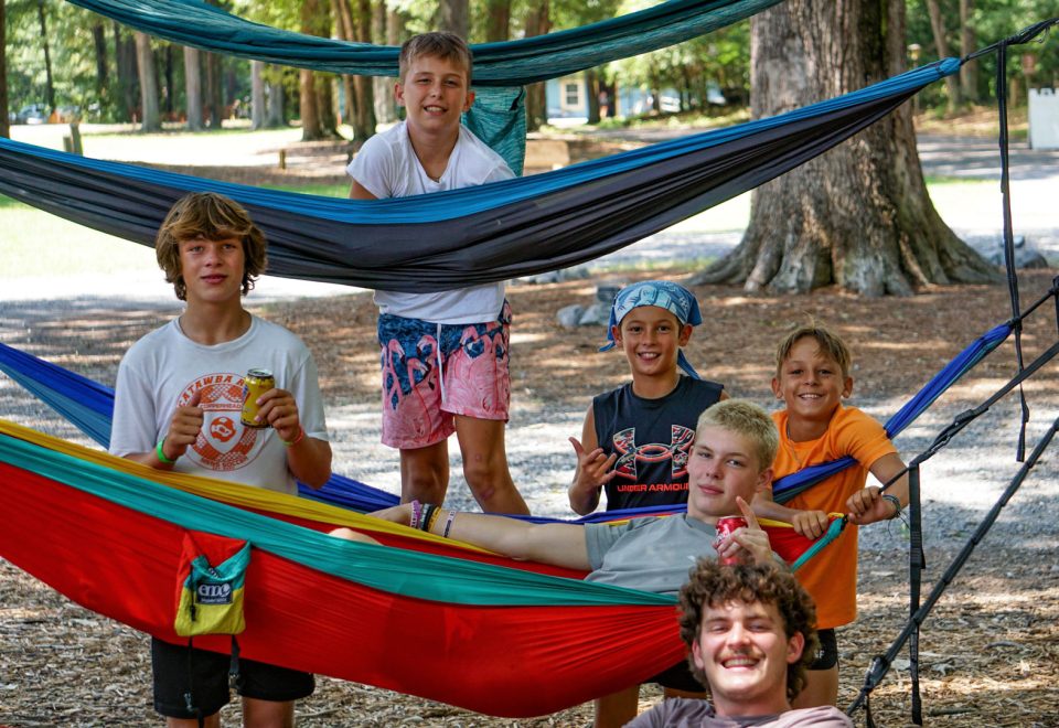 Boys relax in colorful hammocks stacked vertically in trees and a sunny sky in the background during overnight summer camp at Camp Canaan.