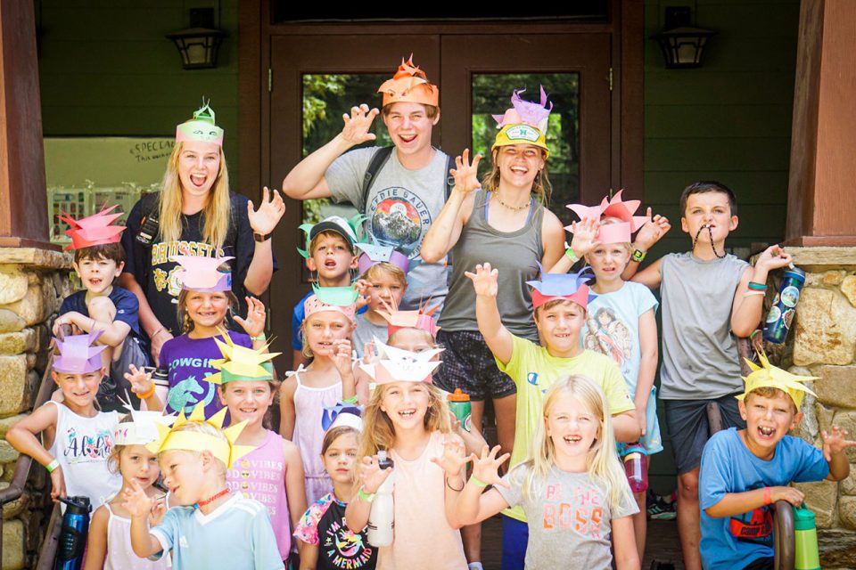 group of junior day campers make a claw with their hands while wearing crafted dino hats from craft time at Camp Canaan