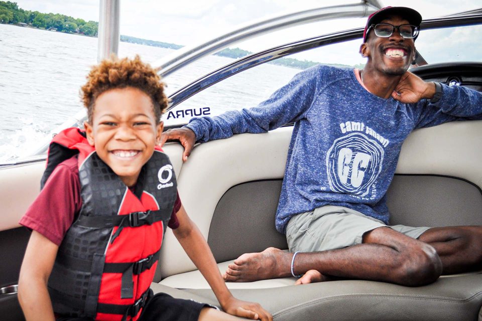 african american counselor smiles while riding next to camper on Camp Canaan's boat