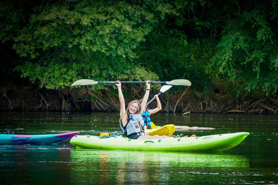 woman with brown hair raises kayak paddle above her head while coasting down the Catawba River in a green kayak