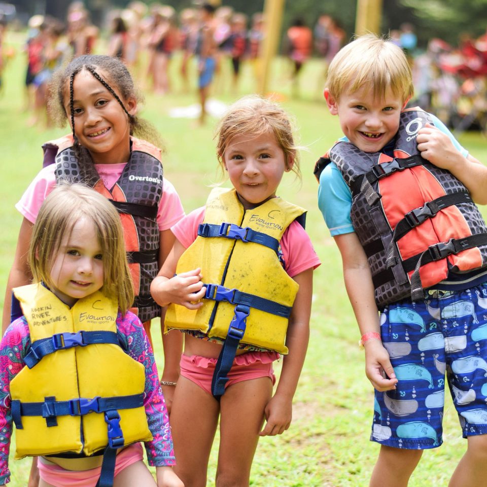 group of smiling junior day campers wearing bright life vests by the lake at Camp Canaan