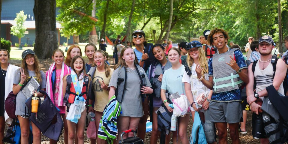 A group of teenage campers and a few counselors, one wearing his life jacket backwards, pose together at Camp Canaan during summer camp.