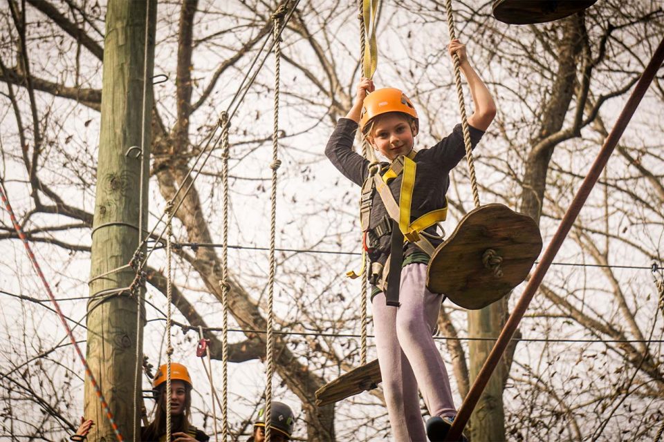 young female camper in orange helmet balances on the high ropes course element at Camp Canaan