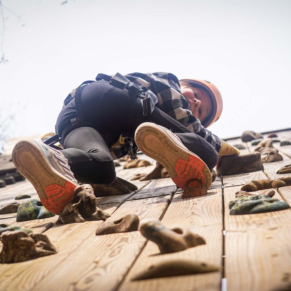 young woman looks down after climbing to the top of the rock climbing wall at Camp Canaan