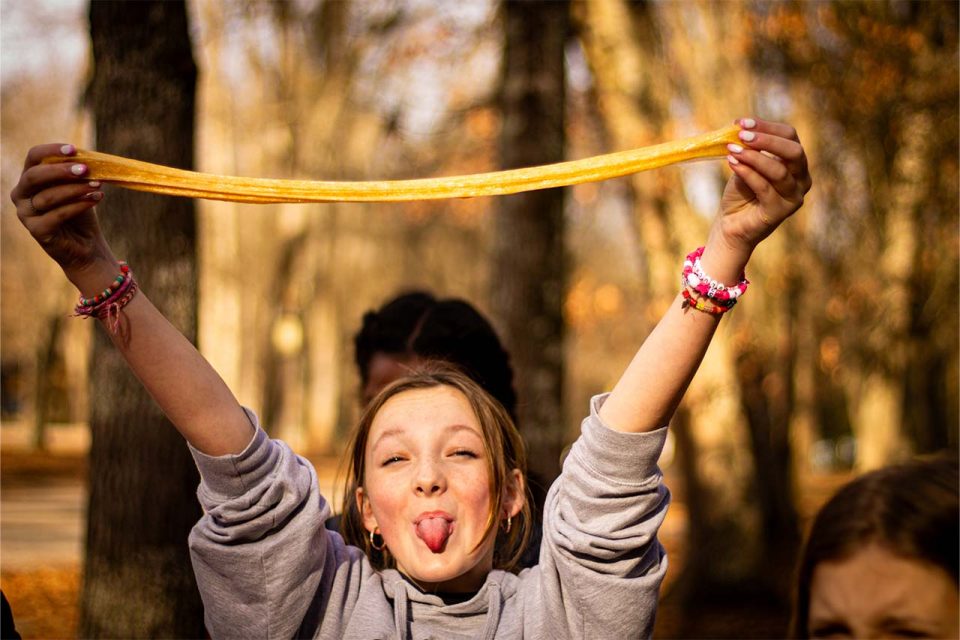 girl camper sticks out her tongue and holds yellow slime above her head