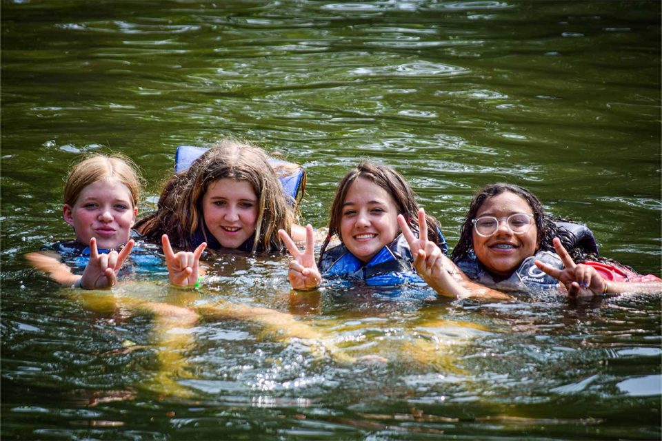 girl campers give peace signs while swimming in lake canaan