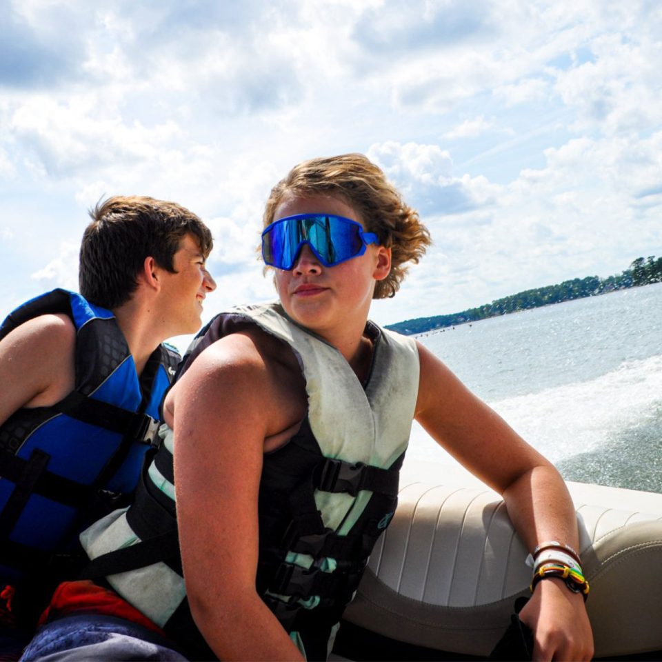 boy camper wearing blue sunglasses looks out at the water from the boat on Lake Wylie