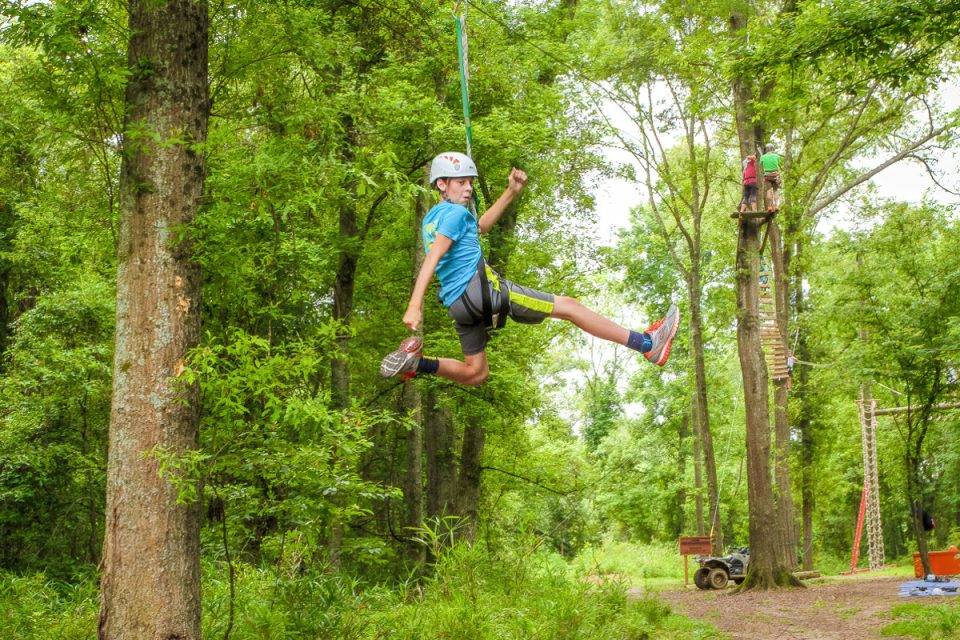 young male camper pretends to run in the air while zipping down the gravity zipline at Camp Canaan