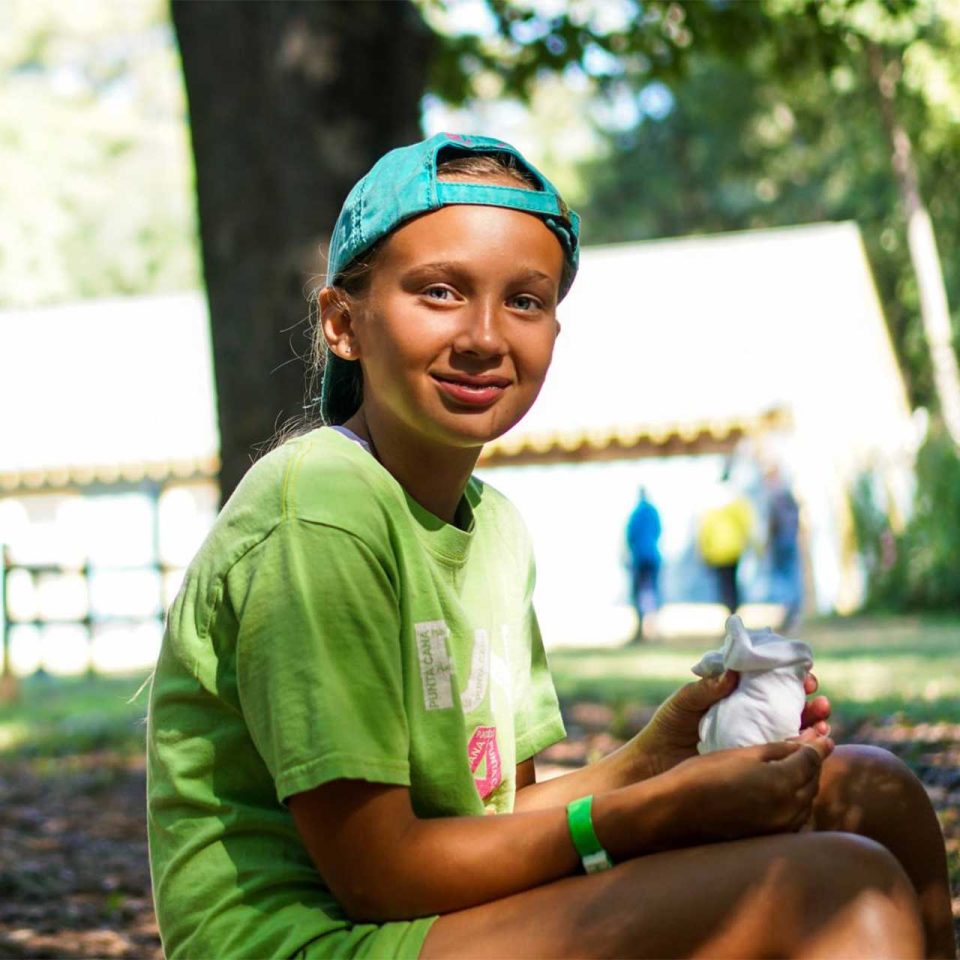 female senior day camper smiles wearing backwards teal hat and green shirt