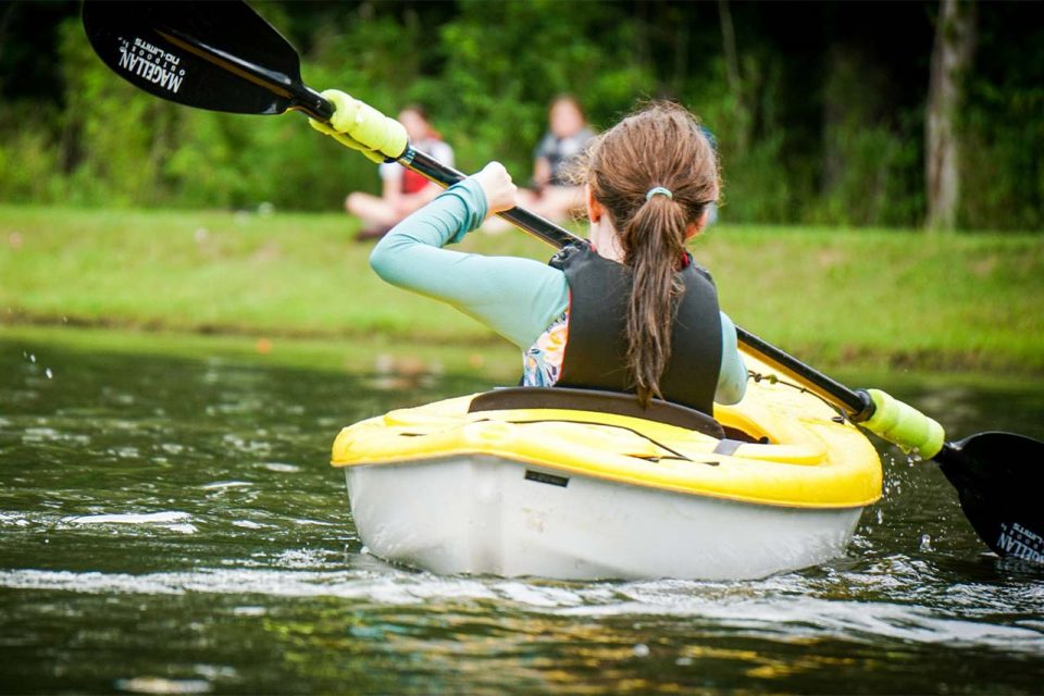 female camper paddles yellow kayak across Lake Canaan during summer camp