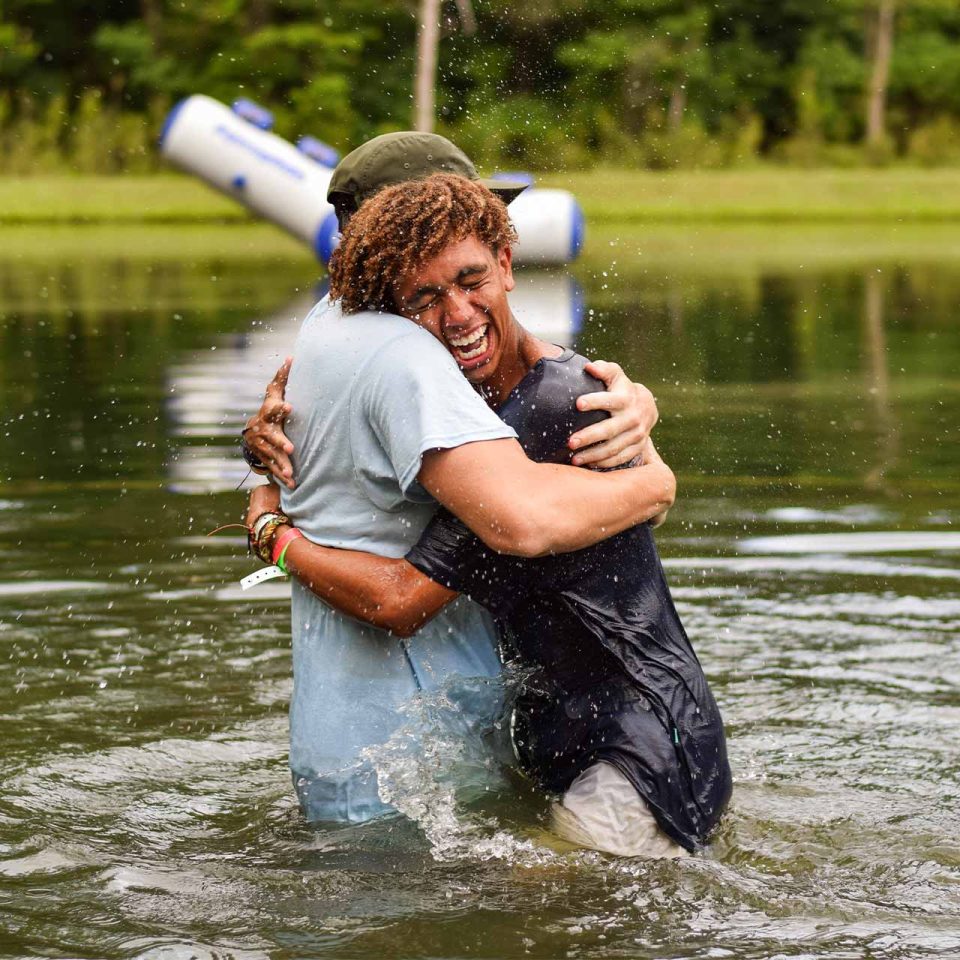 male counselor embraces another male counselor after being baptized in Lake Canaan