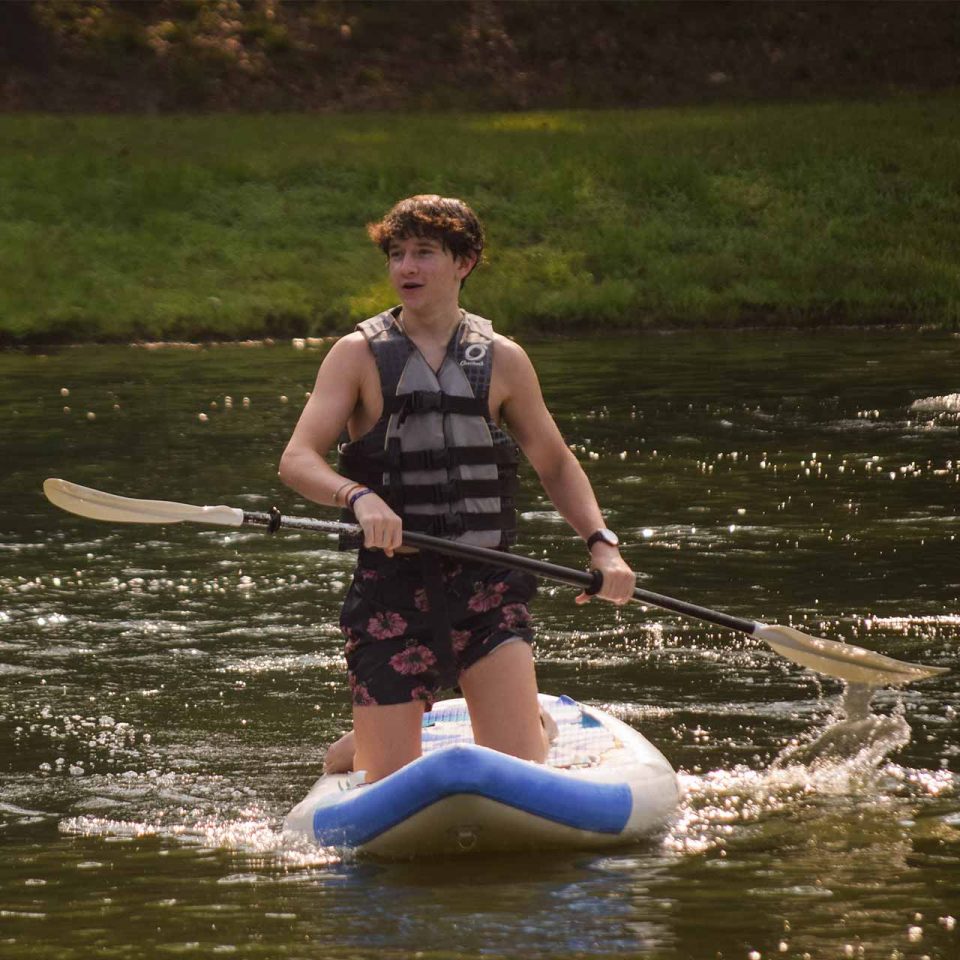 male legacy camper balances on his knees on top of stand up paddle board holding paddle