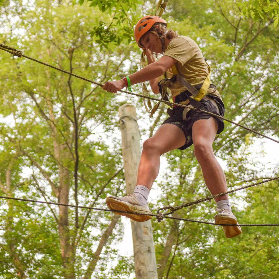 male legacy camper balances on high ropes course element at Camp Canaan