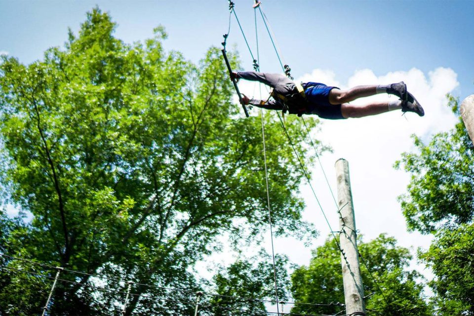 male senior day camper tries the leap of faith element at Camp Canaan and reaches the bar