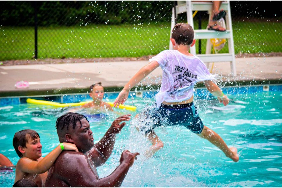 boy camper jumps into swimming pool during summer camp at Camp Canaan