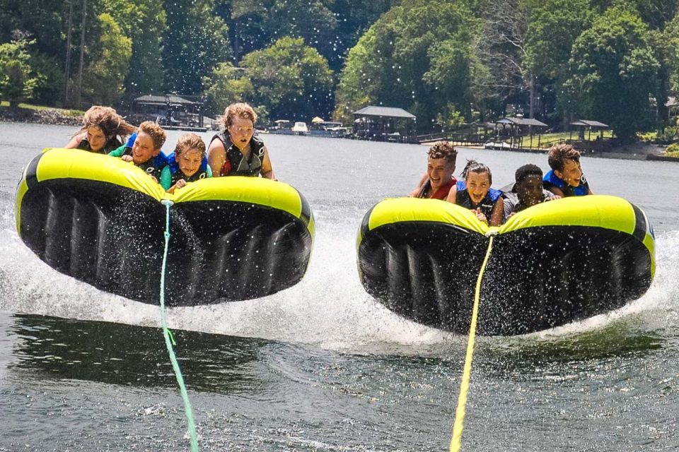 two groups of four kids and counselors tube side-by-side behind the boat in Lake Wylie trying to hold on to the tube