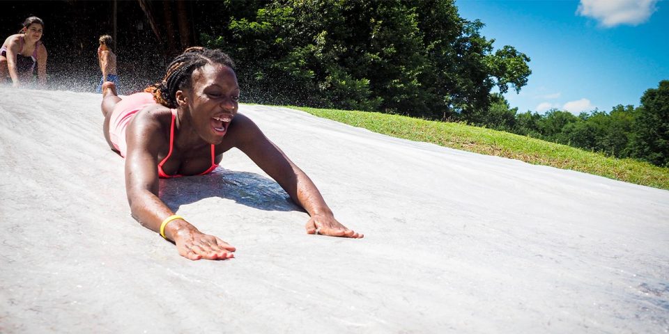 senior day camper with braces smiles while going down the slip n slide at Camp Canaan