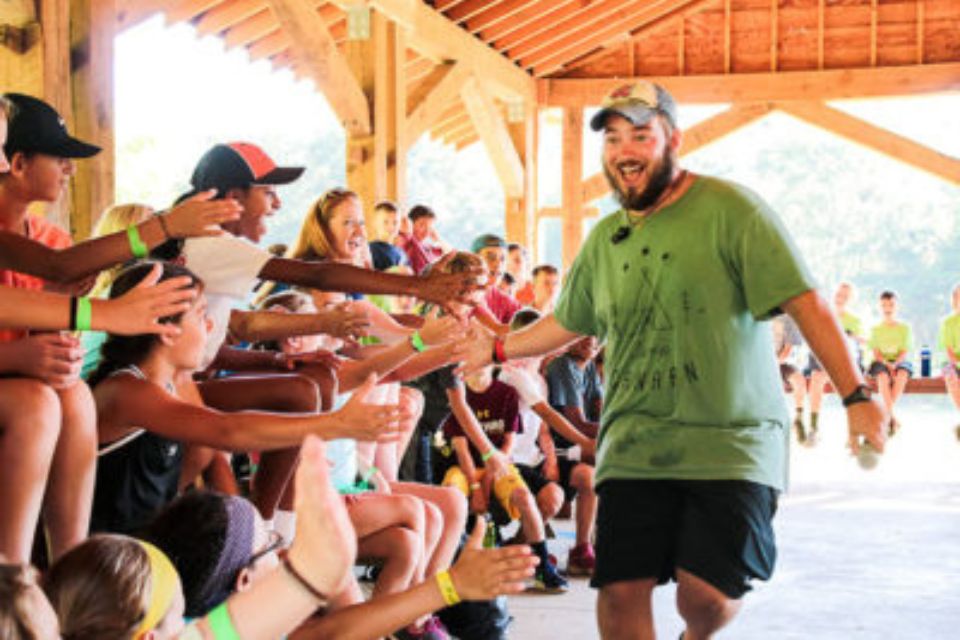 Robbie Conley gives high fives to campers lined up along the side of the picnic pavilion