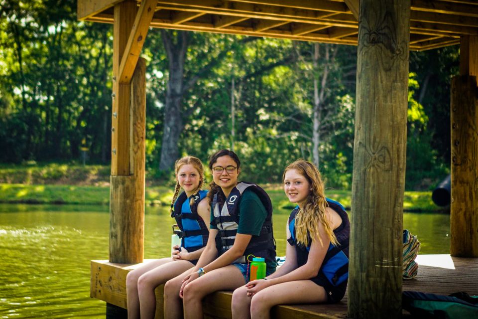 older girl campers sit on dock in life vests dangling their feet in the water