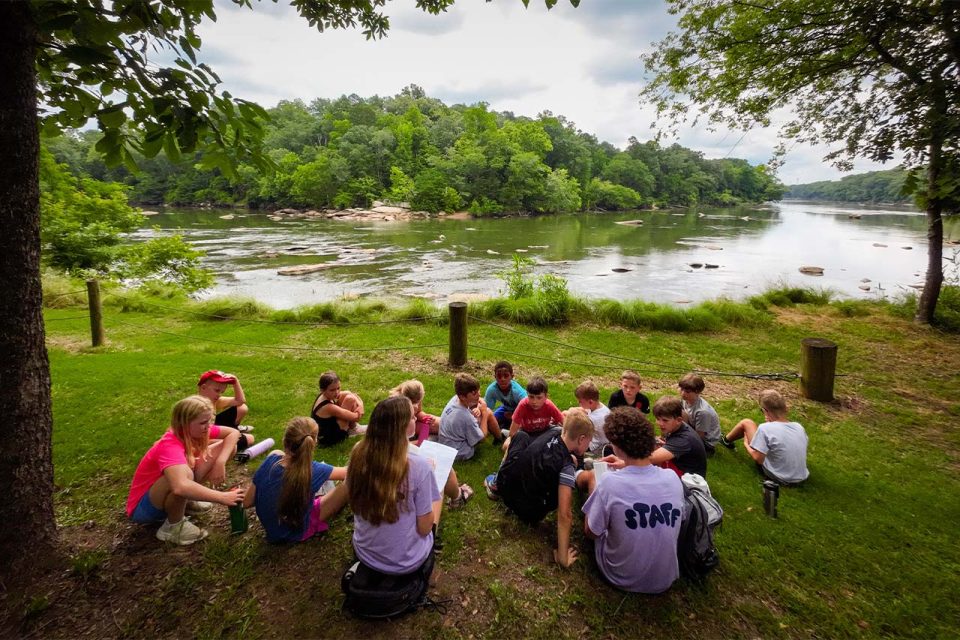 campers circle up near the river's edge to have IOT devotional time