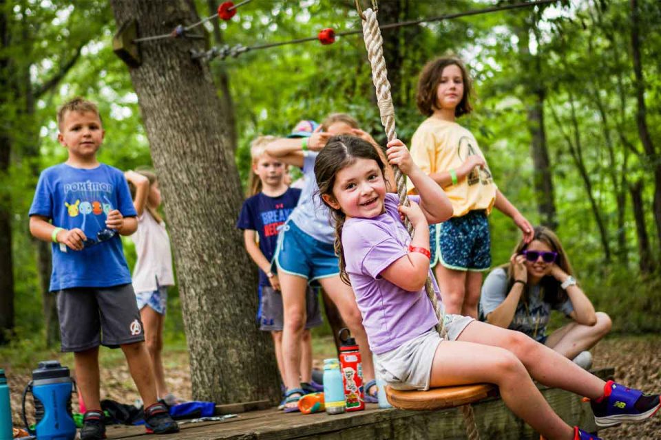 camper in purple shirt rides zipline on playground at Camp Canaan during summer camp