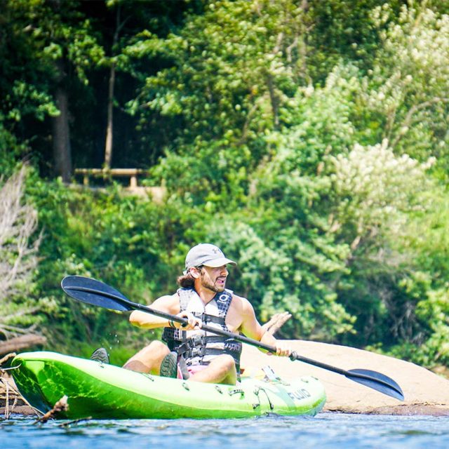 A person wearing a grey hat and life jacket is kayaking on the Catawba river in a bright green kayak.