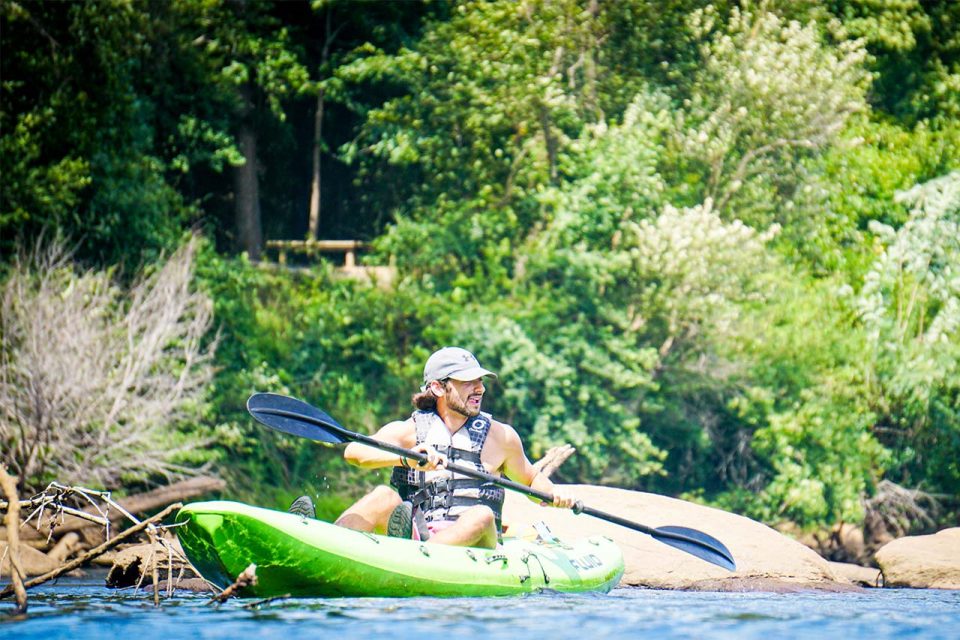 A person wearing a grey hat and life jacket is kayaking on the Catawba river in a bright green kayak.