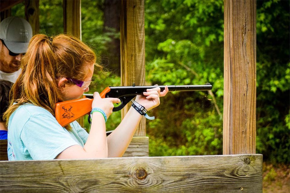 female camper wearing safety goggles does sharp shooting activity during summer camp at Camp Canaan