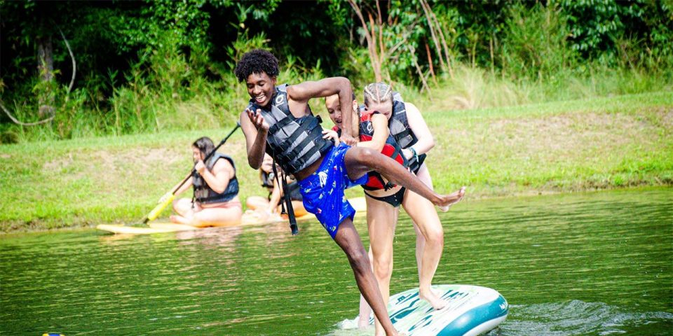 teen camper falls off stand up paddle board during summer camp at Camp Canaan