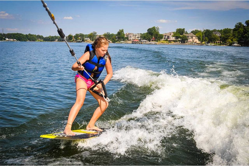 female camper wakeboards behind boat during summer camp